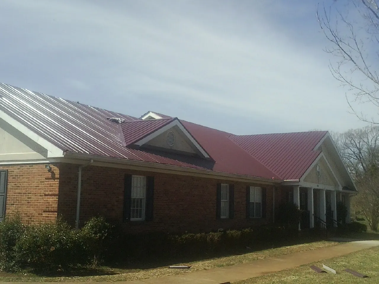 Red metal roof with gabled entries on a long brick building, from a Hail Damage Roof Repair job in Fairfield